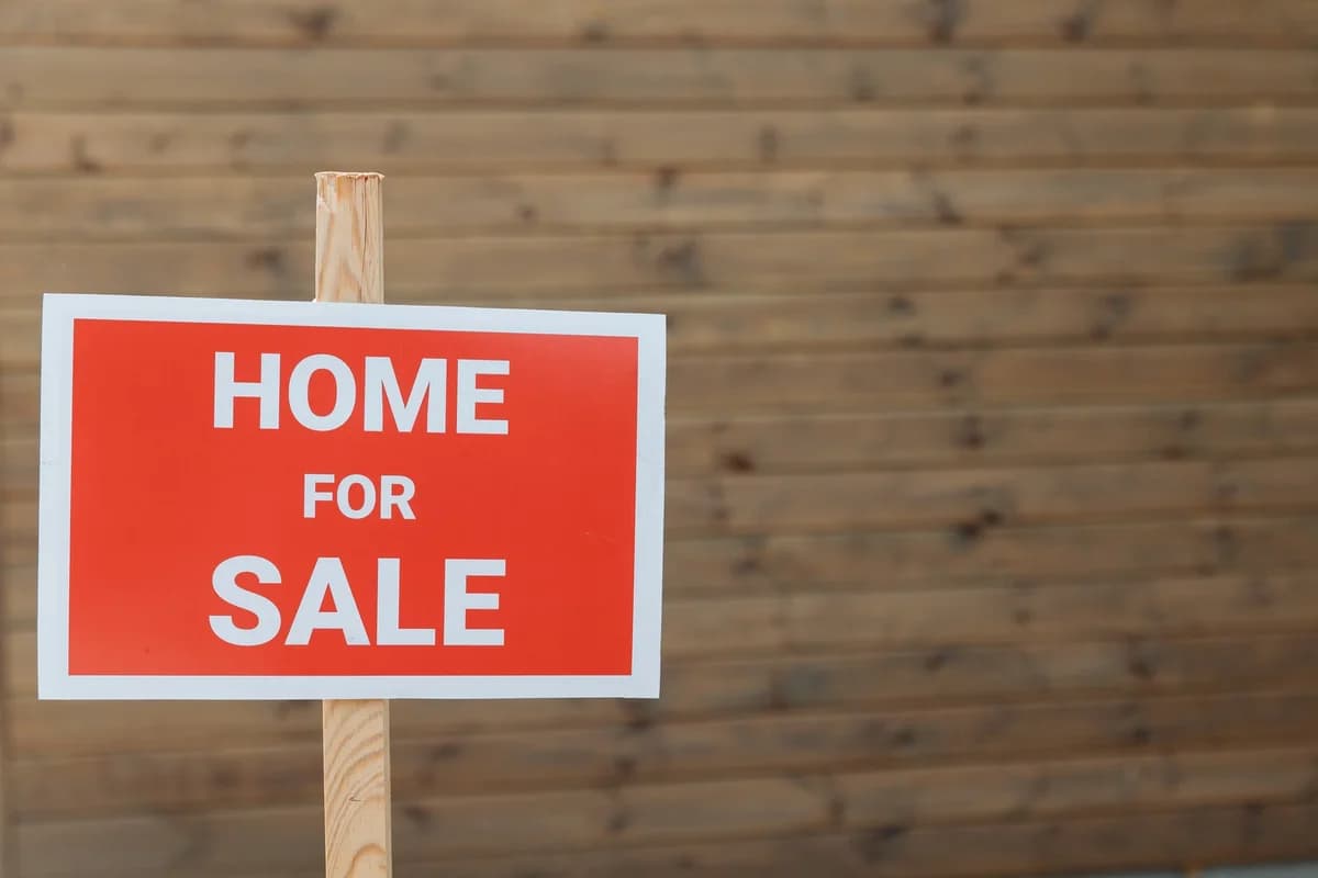 Red home for sale sign on wooden post