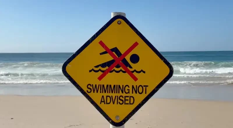 Yellow warning sign on beach saying swimming not advised with red cross over swimmer symbol