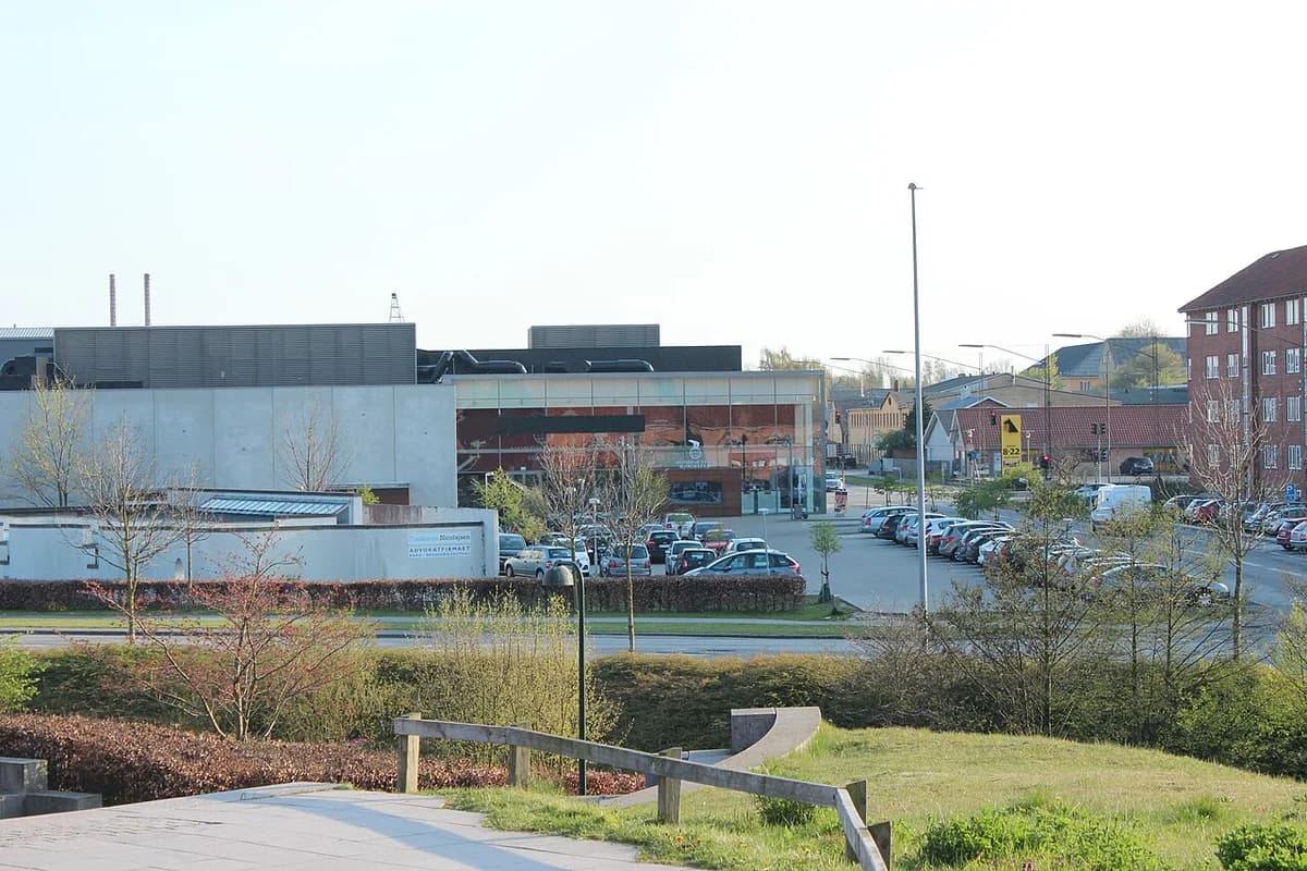 A modern cinema building in Næstved with parked cars nearby.