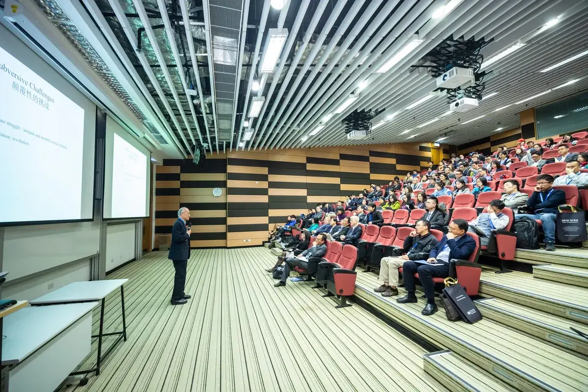 A speaker presents to an audience in a modern lecture hall.