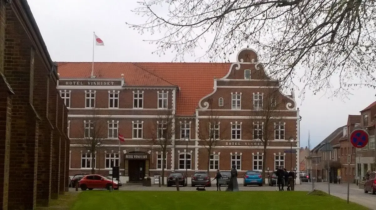 Historic Hotel Vinhuset building in Næstved with parked cars and a few people outside.