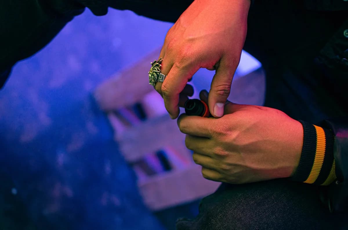 A close-up shot of hands wearing rings, holding a bottle in a colorful setting.