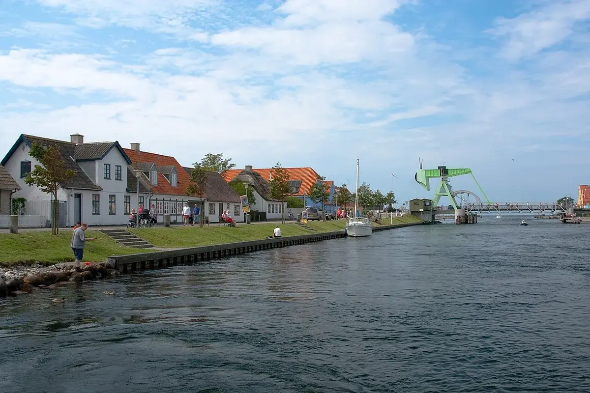 Harborfront in Karrebæksminde, Denmark, with houses, a green drawbridge, boats, and people by the waterfront.
