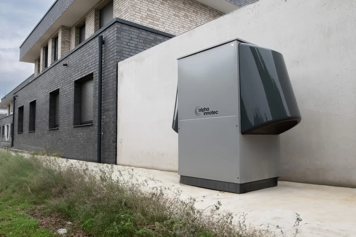 An alpha innotec heat pump installed outdoors next to a modern building.