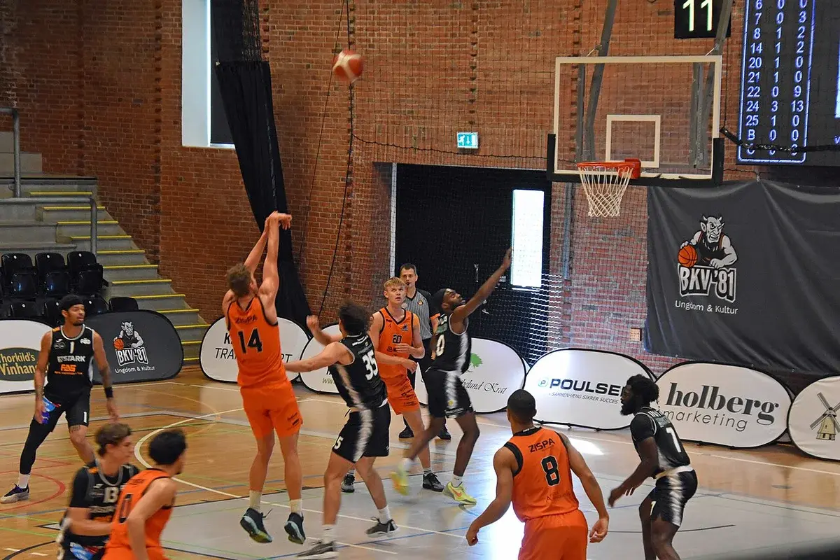 Indoor basketball game with players contesting a shot near the basket.