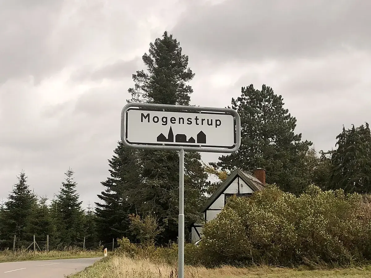 Road sign for Mogenstrup beside a rural road.
